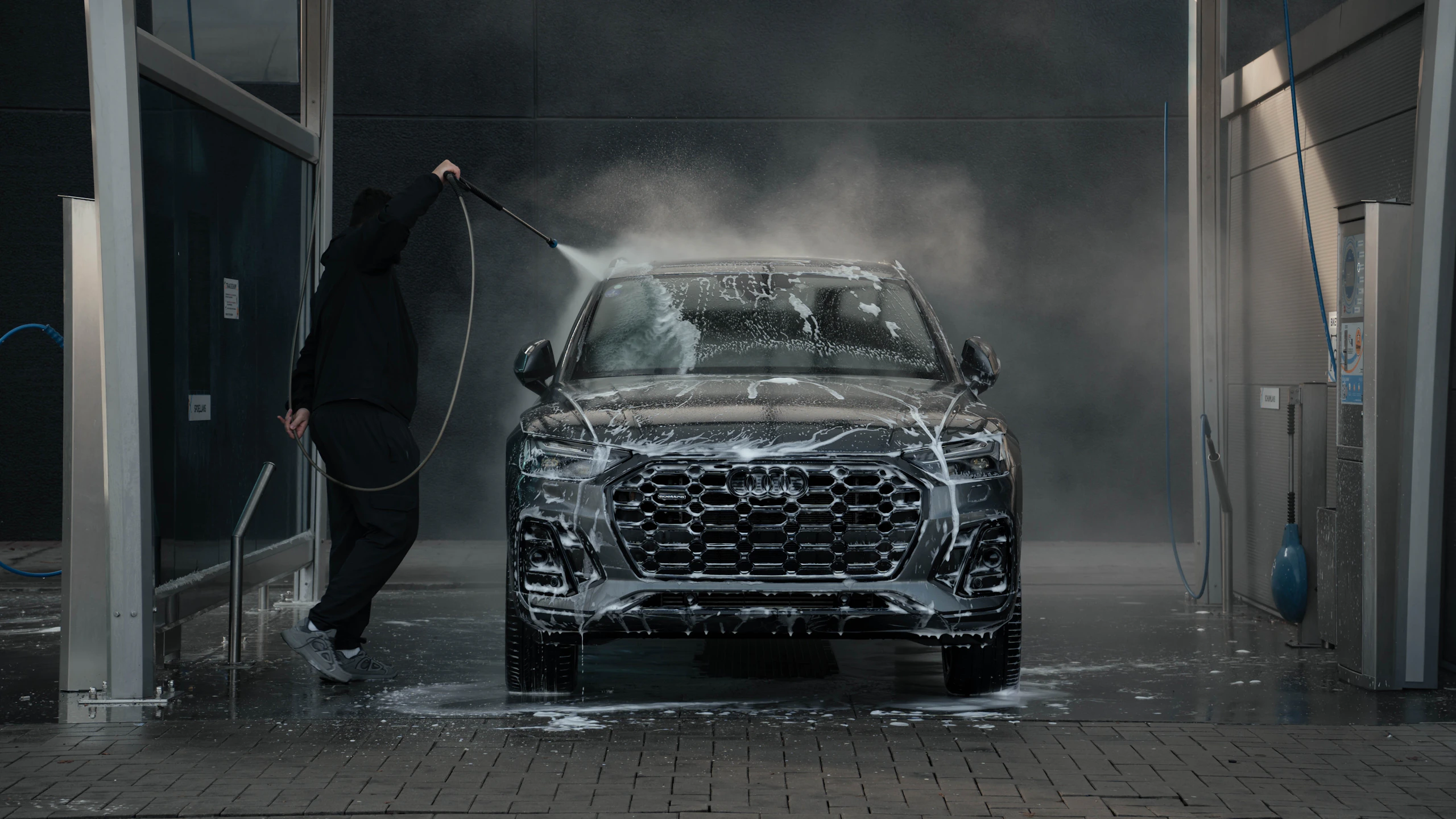 A dark SUV being carefully pressure washed in a car wash bay